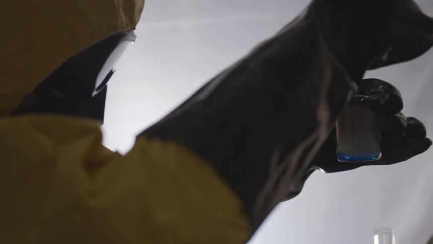 Individual in a hazmat suit shakes chemicals in a beaker