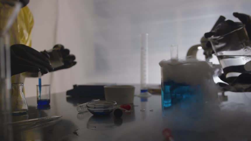 Two people in hazmat suits and gloves are handling blue smoking materials