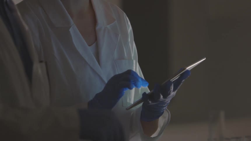 Two people stand together while one picks up a test tube and the other types on an electronic device