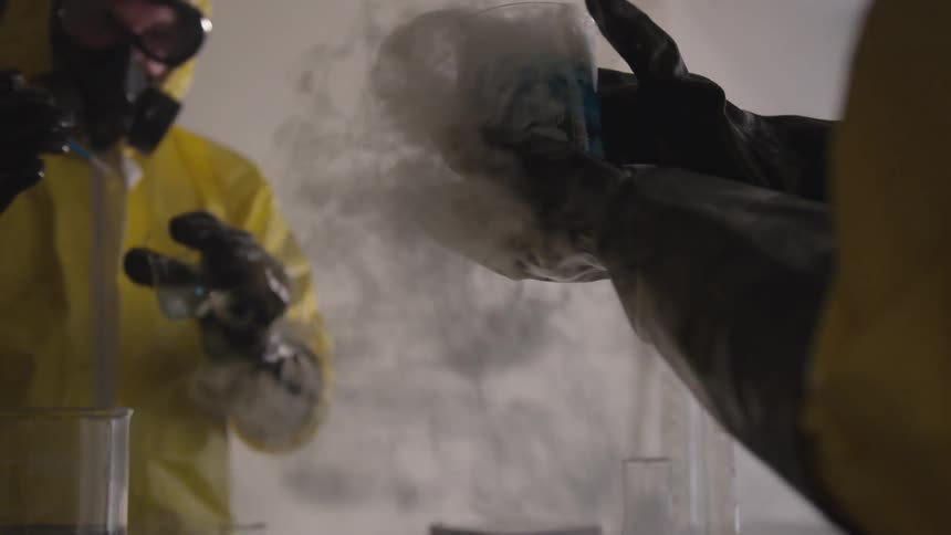 Two people in yellow hazmat suits experimenting on a blue liquid