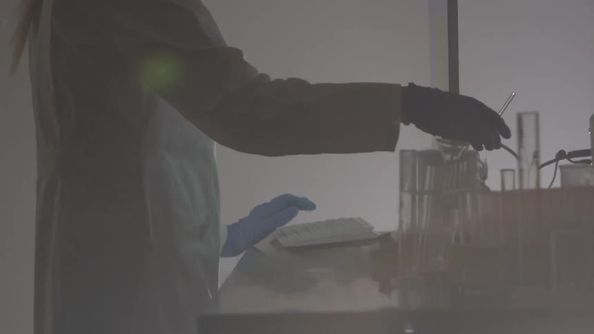 Female scientist types on a keyboard then grabs a glass swizzle stick and stirs a mixture in a container