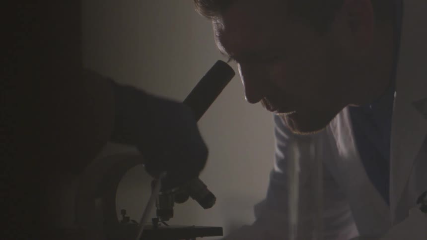 The scientist is looking into the microscope as his assistant annoys his view