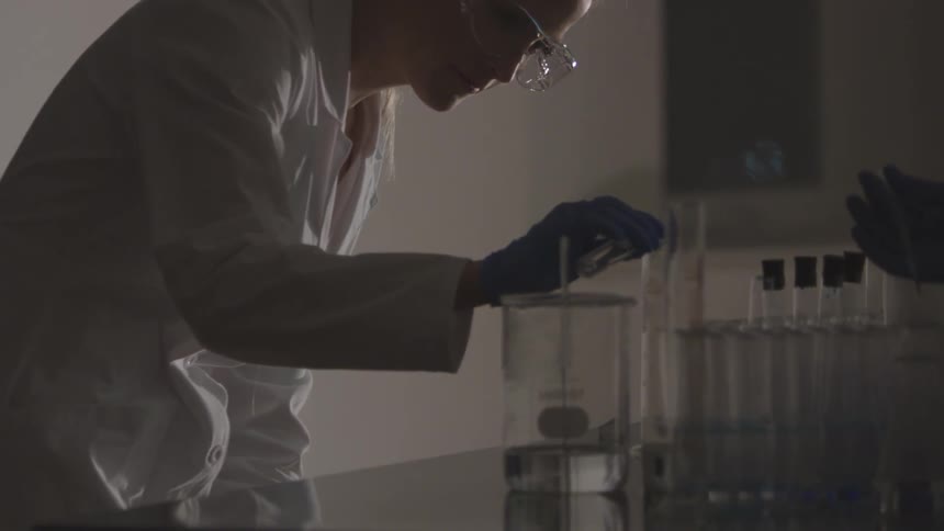A person wearing personal protective equipment manipulates fluids in test tubes