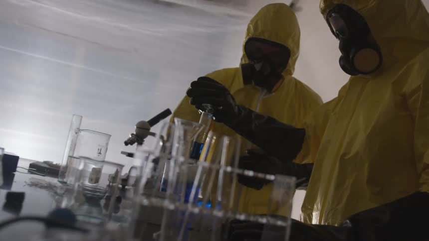 Two people in yellow hazmat suits experimenting on a blue chemical