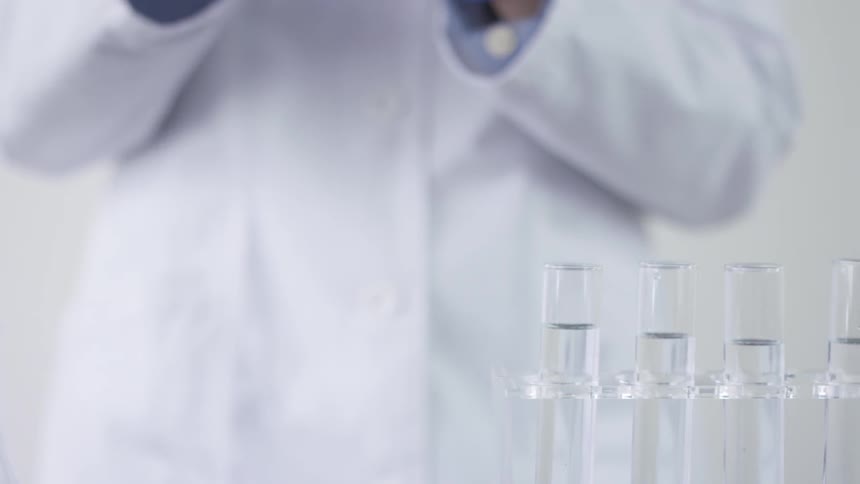 Tubes of clear liquid with a person in a white lab coat in the background