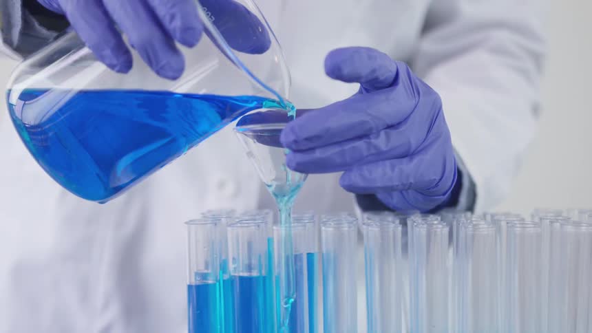Scientist pours blue liquid from beaker into test tube using glass funnel