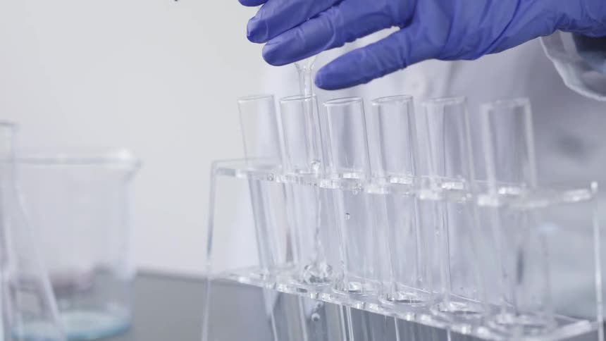 Person in gloves and a lab coat pours liquid into test tube