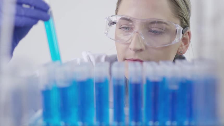 Female chemist lifting up a blue test tube and observing it