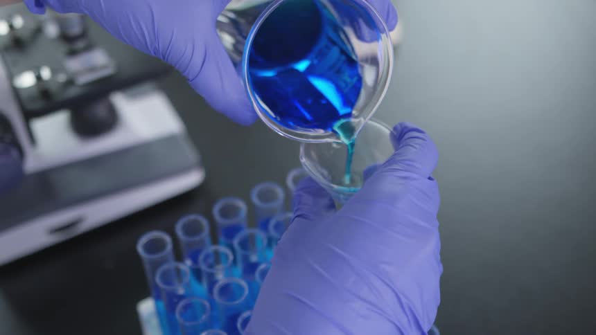 Person pouring a blue liquid from a recipient to another one in a laboratory