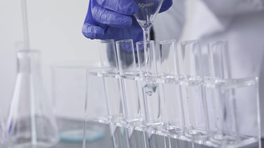 Chemist pouring liquid through a glass funnel to a glass tube