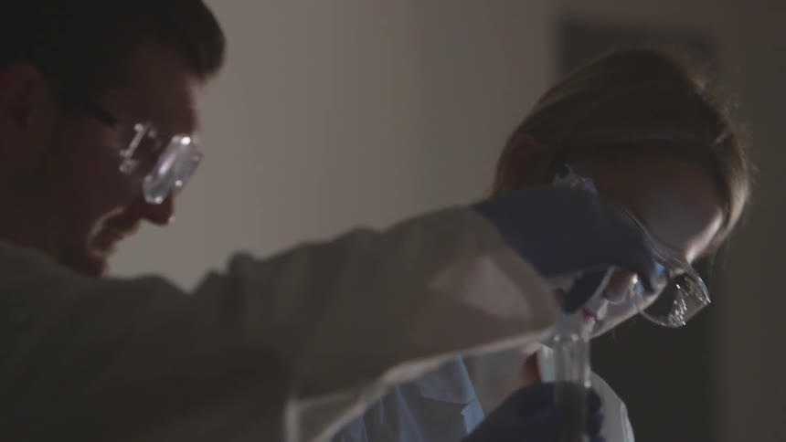 A male and female chemist stirring the contents of a beaker