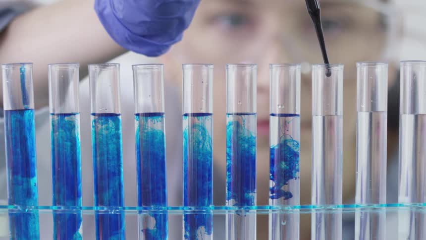 A woman uses a dropper to put a blue solution in test tubes