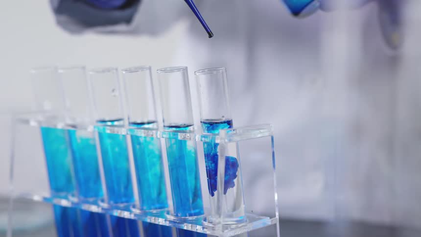 A chemist squeezing drops of a blue liquid into beakers of water