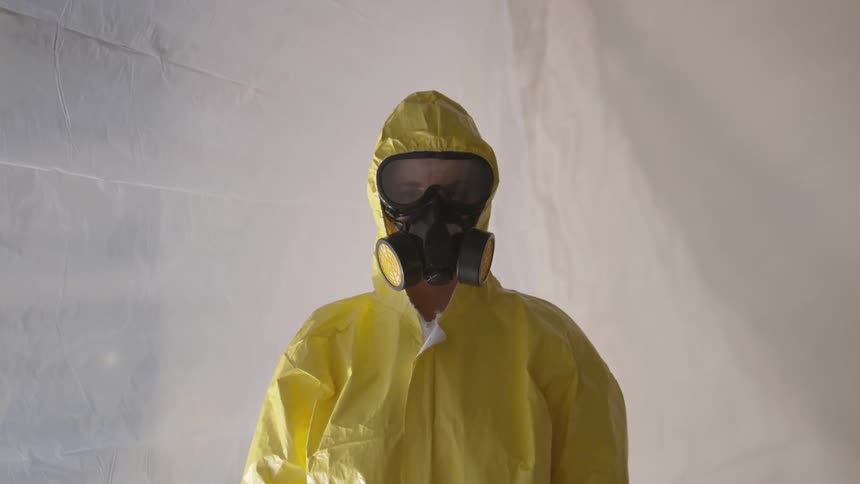 A person wearing a gas mask and a yellow laboratory safety suit