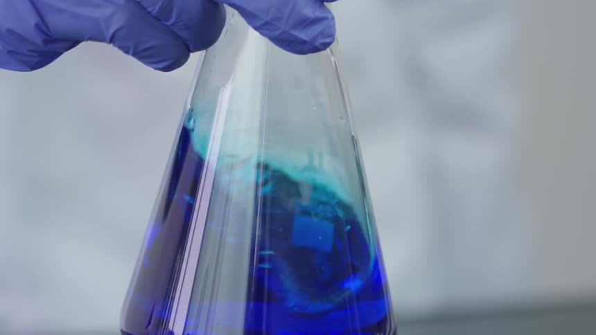 A person swirls a blue solution in a beaker