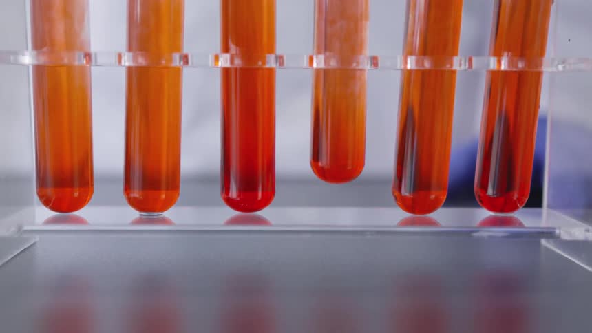 A vial containing a reddish orange liquid being lifted from among a set of similar vials