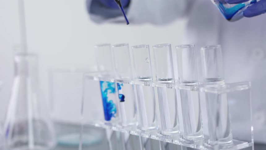A person dropping one drop of blue liquid in tubes of clear liquid