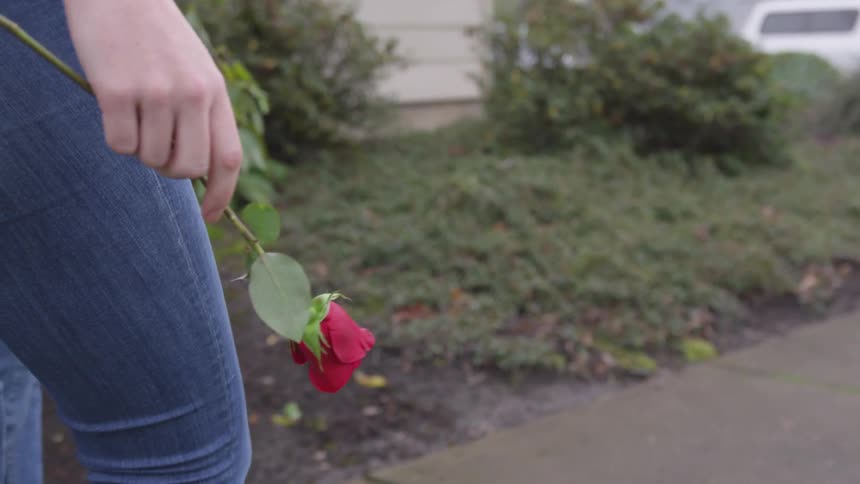 A female walking down the sidewalk holding a rose