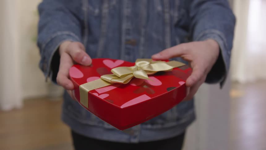 A person holding out a heart shaped red box with a box