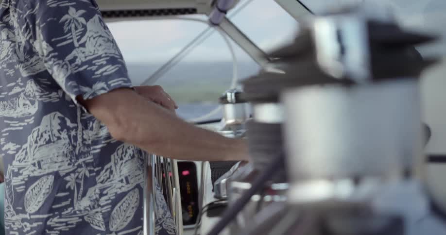 A man stands at the helm of a yacht manipulating the controls