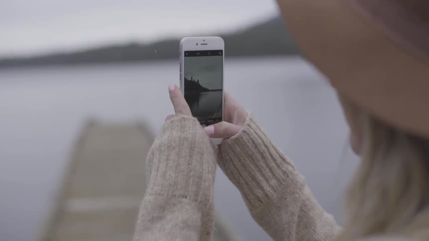 Woman takes a picture of a lake with a camera phone