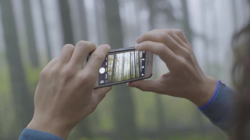 A person taking a photo on a smartphone in the forest