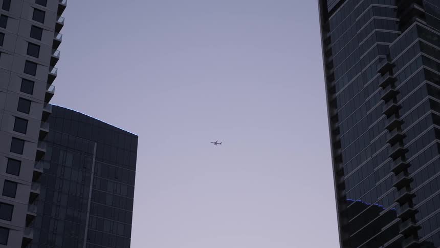 A plane flies across the sky framed by buildings
