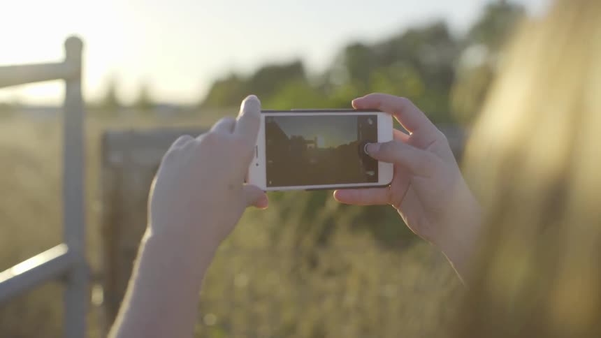 Girl takes picture of sunset while the sun goes down in the rural area