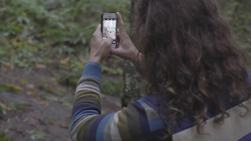 A man taking a picture of the forest with his phone