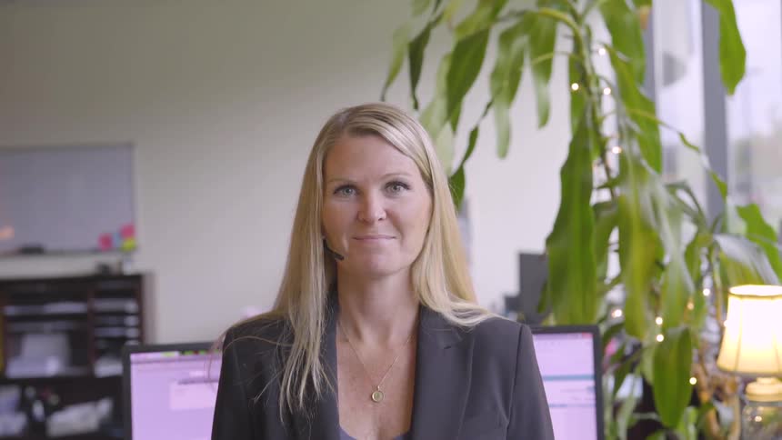 A woman in an office with monitors and a plant in the background