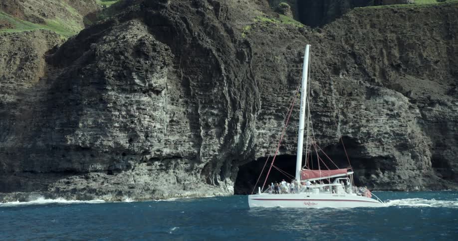 A crowded sailboat near a sea cave