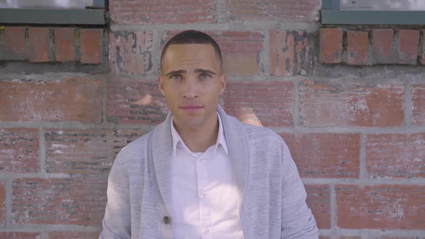 Man who stands in front of the wall between two windows turns his head to the camera by day