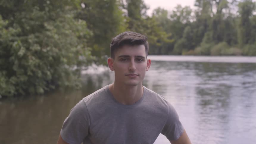 A young man stands in front of a lake