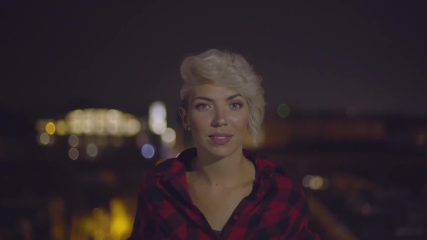 A woman standing on a balcony over a street at night