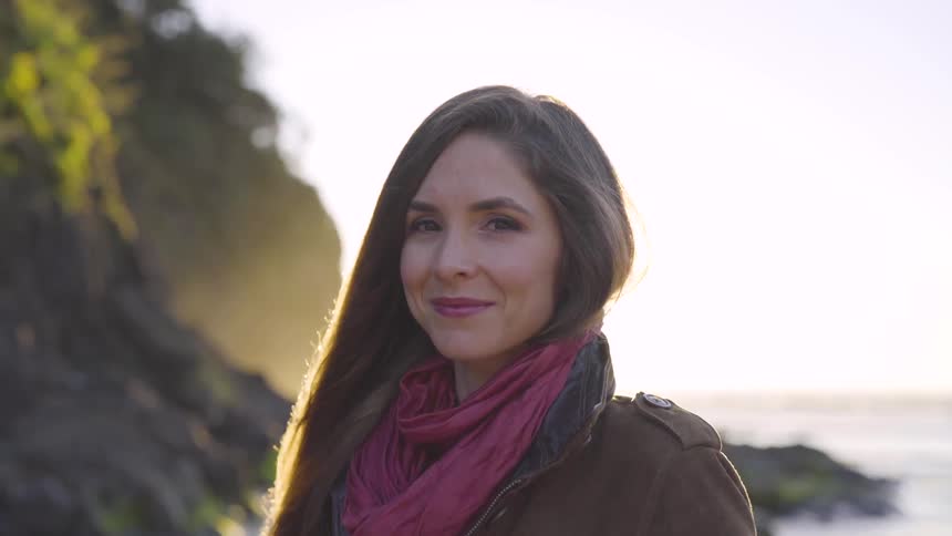A woman with long hair wearing a scarf standing by the ocean