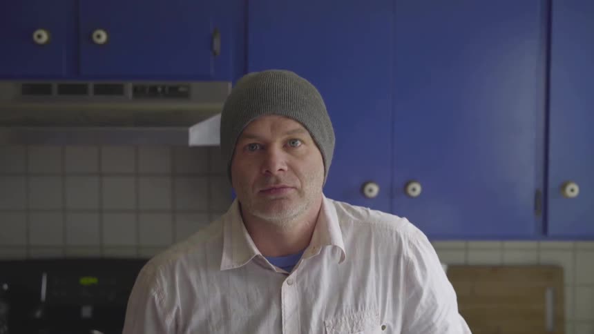 Man in blue kitchen looks up and stares ahead