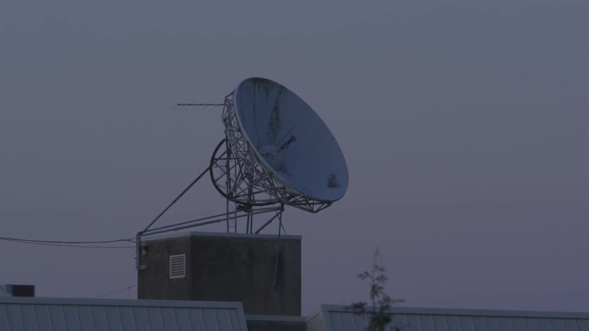 A satellite dish receiver stands on top of a building pointing towards the dark sky