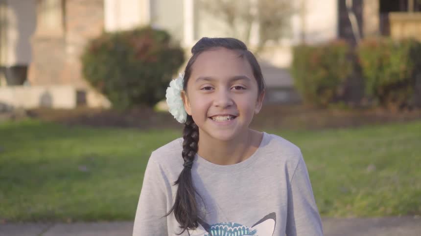 A young girl sitting in a front yard smiling