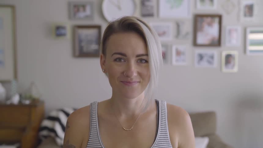 A white woman with short blonde hair in a striped shirt is smiling in a room that has pictures all over the wall