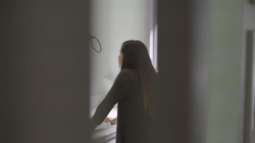 A woman stands at a sink looking down