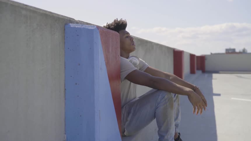 Young black man sits on a concrete wall and pulls his hair