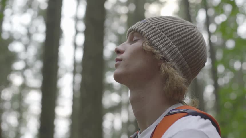 Young man meditating with closed eyes at the middle of a forest