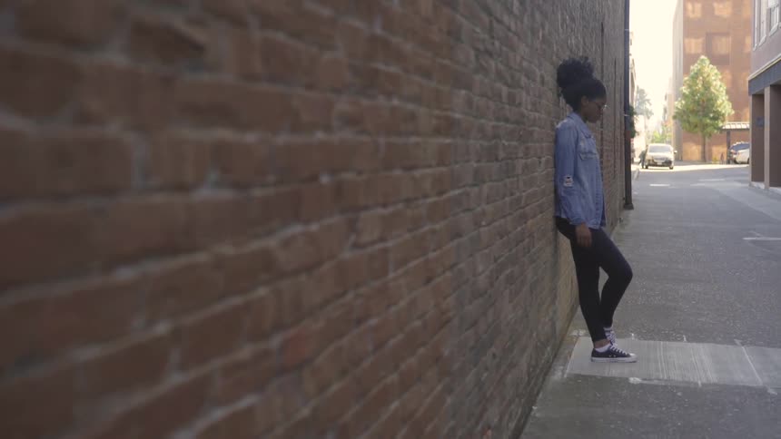 A female standing up against a brick wall in an alley