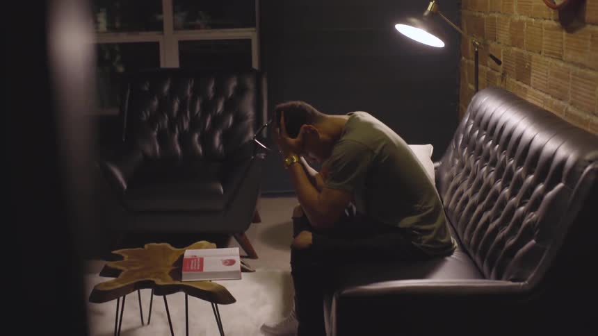 A man sitting down on a couch and putting his head in his hands