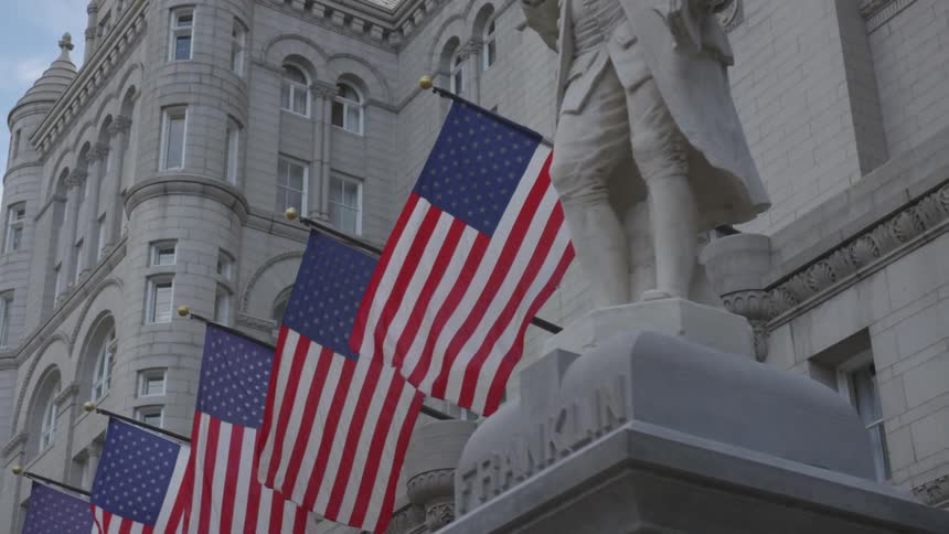 American flags are hanging from a marble building and blowing in the breeze