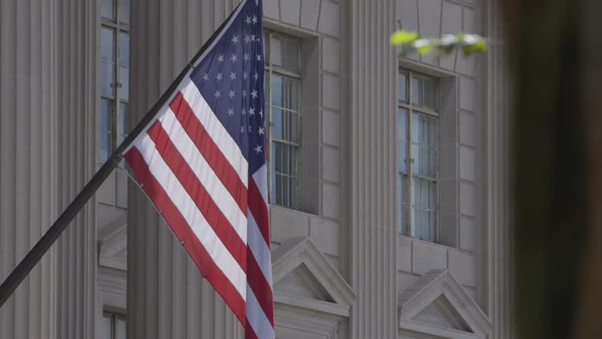 A red white and blue american flag hangs on a pole outside a building with several rectangular windows
