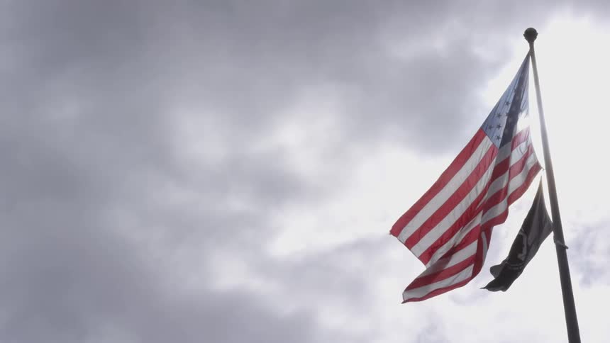 An american flag and a pow flag blowing in the wind