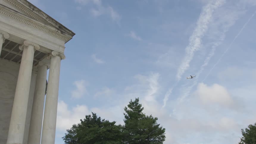 A plane flies across the sky with a building in foreground