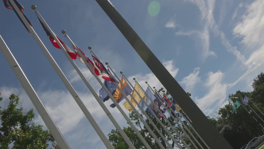 With a blue sky behind them flags on flagpoles waving slowly in the wind shot at an angle