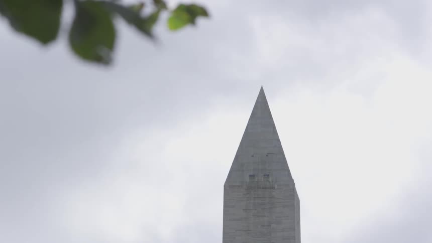 The pointed top of the washington monument stands against the backdrop of a blue but cloudy sky